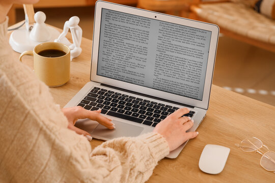 Female writer editing manuscript on laptop before publishing in office