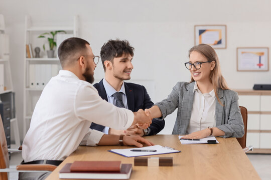 Male business mediator shaking hands with clients at table in office