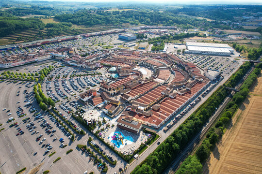Aerial view of Designer Outlet Serravalle featuring red-roofed shops, extensive parking lots, and a small water park in Serravalle Scrivia, Piemonte, Italy.