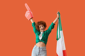 Fototapeta premium Female soccer fan with Italian flag and foam hand on orange background