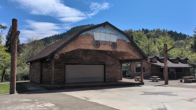 Video of rustic outdoor stage with covered wagon artwork and western-inspired wooden buildings surrounded by trees in rural Oregon.