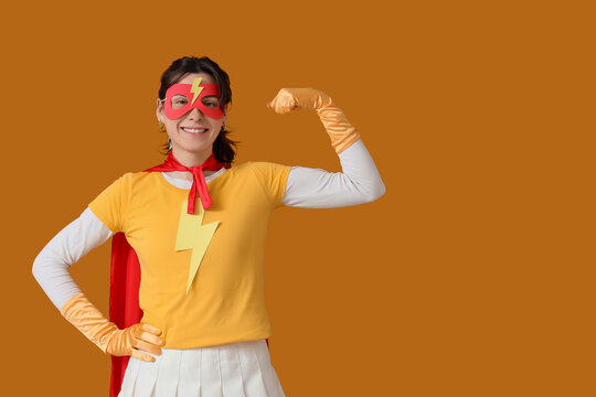 Young woman in superhero costume showing muscles on orange background