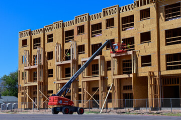 Construction workers using a telescopic boom lift at an apartment building under construction, representing elevated access work, structural assembly, and multifamily housing development © Eduardo Barraza