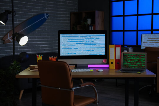 Computer monitor and laptop with codes on programmer's desk in dark office