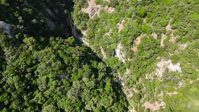Aerial Drone View of Hidden Waterfall in Polylimnio Canyon, Greece, Surrounded by Dense Mediterranean Forest and Rocky Gorge Cliffs