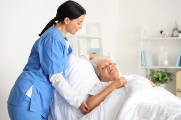 Naklejka premium Female nurse putting senior woman to bed in bedroom