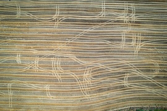 Aerial view of a harvested agricultural field featuring intricate tractor tire tracks across golden straw stubble in Carignano, Piemonte, Italy.
