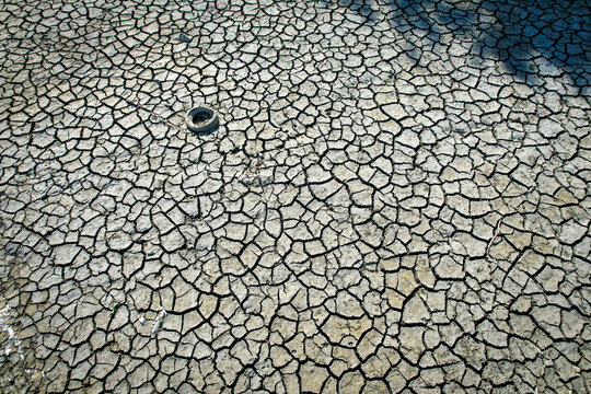Aerial view of cracked dry earth and parched soil during a severe drought with a discarded tire Carignano, Piemonte, Italy.