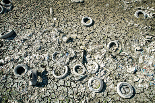 Aerial view of discarded tires and plastic trash scattered across a parched and cracked riverbed during a drought in Carignano, Piemonte, Italy.