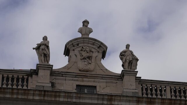 Palacio Real de Madrid in Comunidad de Madrid Spain features stone statues and royal coat of arms on balustrade above facade representing Bourbon monarchy architecture, upwards shot