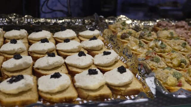 Assorted tapas at Mercado de San Miguel Madrid Spain include bread canapes topped with fish roe caviar and seafood mixtures presented in deli trays, lateral pan to right reveal