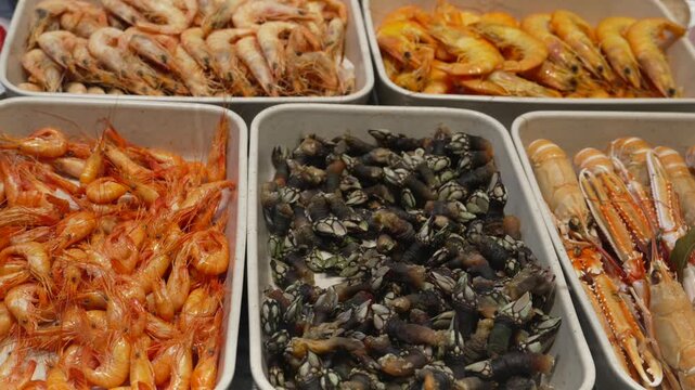 Assortment of fresh seafood including prawns, barnacles, and langoustines displayed in serving trays, offering variety at San Miguel Market in Madrid, Spain, vertical pan downwards