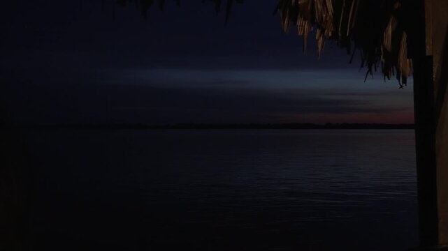 Canoes rest under a thatched structure at twilight, with a view of the calm Amazon River. Ideal for scenes depicting tranquility or travel in remote locations.
