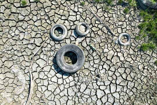 Aerial view of discarded tires on dry cracked earth during a severe drought in Carignano, Piemonte, Italy.