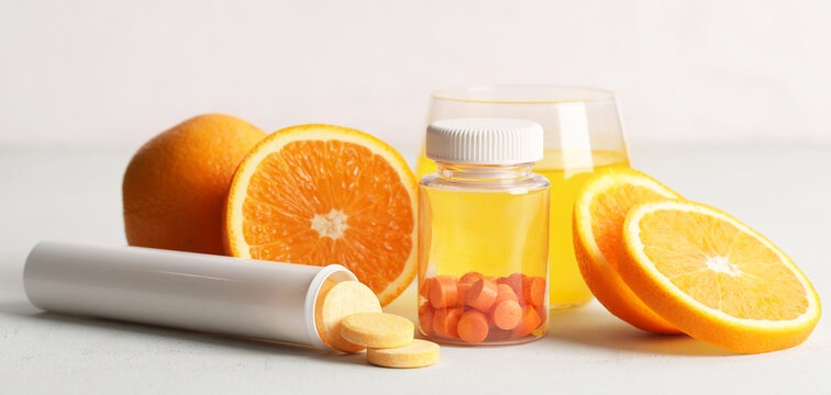 Glass of vitamin C water, soluble tablets and fresh oranges on white table