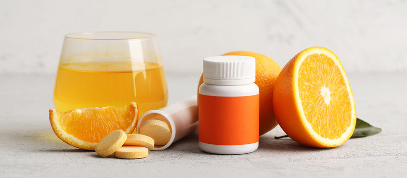Glass of vitamin C water, pills, soluble tablets and fresh oranges on grey table