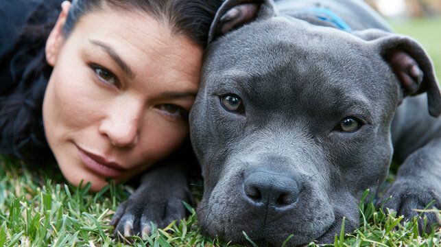 Close up of woman and gray dog lying on green grass, showing calm and affectionate connection in outdoor setting