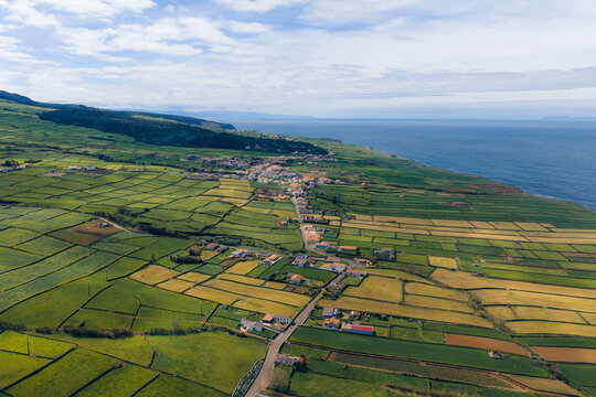 Aerial view of Terceira Island with its characteristic green patchwork fields and a coastal village under a cloudy sky Azores, Portugal.