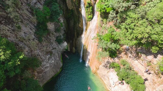 Aerial Drone Approach to Polylimnio Waterfall with Turquoise Pool, Swimmers and Rocky Canyon in Messinia, Greece