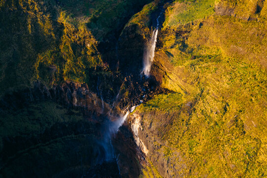 Aerial view of Poco da Ribeira do Ferreiro waterfall cascading down steep green cliffs during golden hour in Fajazinha, Azores, Portugal.