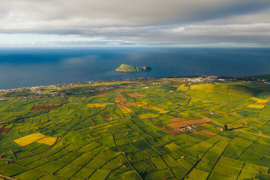 Aerial view of Pico Dona Joana volcanic cone and lush green patchwork fields overlooking the Atlantic Ocean and Ilheu de Cabras Feteira, Acores, Portugal.