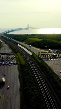 Vertical video. Malmo, Sweden. The Oresund Bridge toll plaza and cable-stayed span stretching across the strait toward Denmark, Drone footage over green coastal terrain at golden hour.. Drone footage