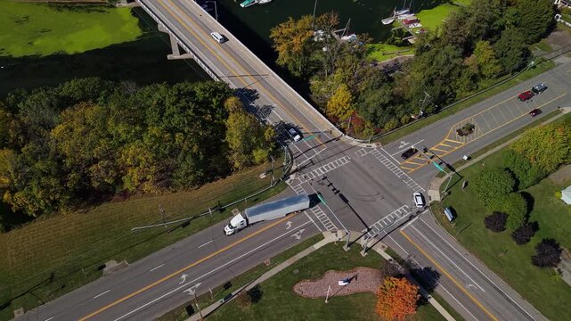 Aerial overhead shot of a long white semi-trailer truck making a wide left turn at an intersection with a bridge and water nearby.