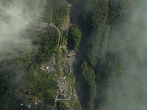 Aerial view of Tambang Pasir Merapi Kali Gendol Sand Mine with a winding road and lush green forests through the mist in Kecamatan Cangkringan, Daerah Istimewa Yogya, Indonesia.