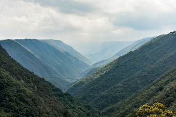 Fototapeta premium Mawkdok Dympep Valley with misty green hills and dramatic cloudy sky, showcasing breathtaking natural landscape in Meghalaya, India.