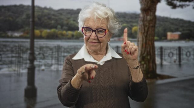 Senior woman points index finger up and points forward with other hand on wet street by a lake; confidence guidance.