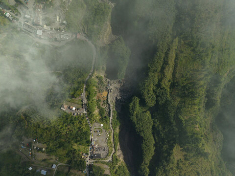 Aerial view of Tambang Pasir Merapi Kali Gendol Sand Mine with deep ravines, lush vegetation, and buildings under a light mist in Kecamatan Cangkringan, Daerah Istimewa Yogya, Indonesia.
