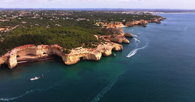 Wide aerial panorama of cliffs at the Benagil caves in Algarve, Portugal. Drone shot, boats on the water, European tourism hotspot