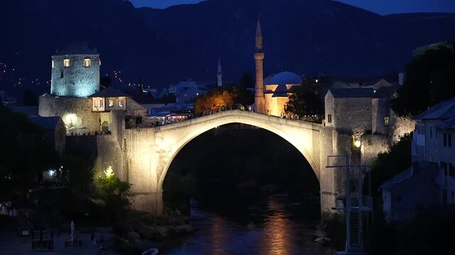 Night shot of Stari Most bridge with tourists walking around.