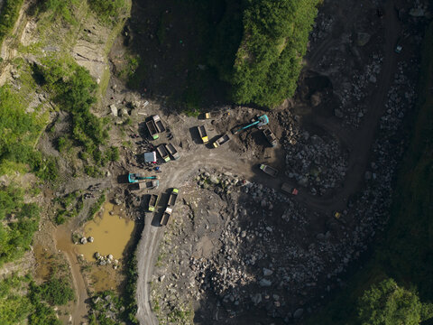 Aerial view of Tambang Pasir Merapi Kali Gendol Sand Mine with excavators and trucks on dirt paths near a pond in Kecamatan Cangkringan, Daerah Istimewa Yogyakarta, Indonesia.