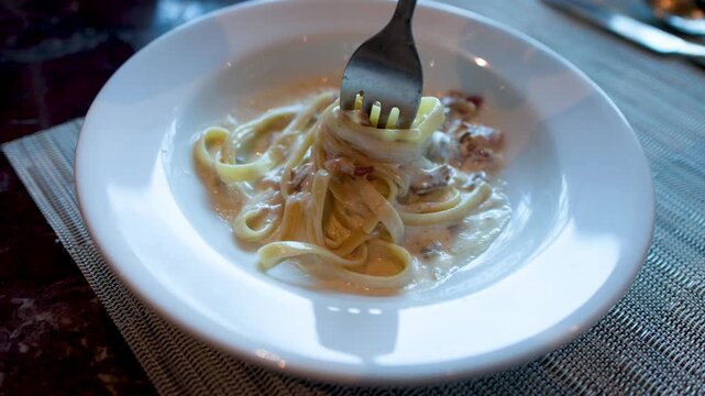 Twirling Creamy Fettuccine Carbonara with a Fork in a White Bowl