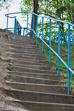 Concrete Stairs Leading Uphill with a Blue Metal Handrail in a Park with green trees.