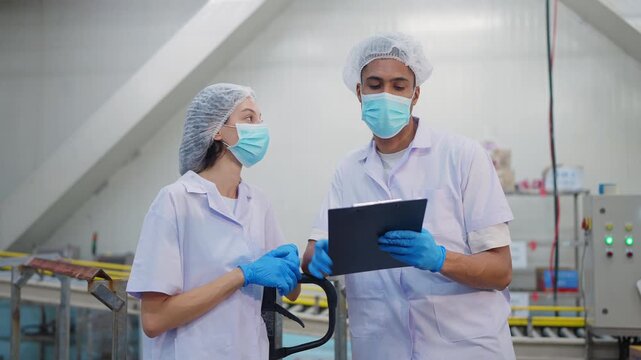 Food production review: Two food industry professionals collaborate during an inspection, wearing protective gear amidst the clean industrial setting.