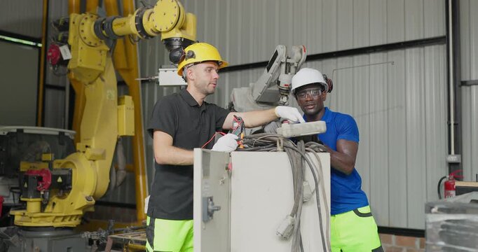 Technicians troubleshoot robotic arm control systems in a workshop, checking settings, electrical components and maintenance data for automation upgrade.
