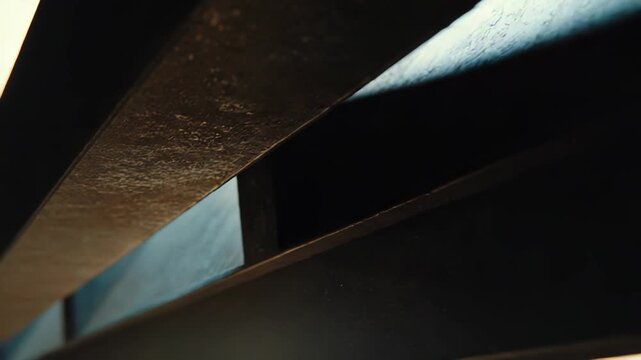 Abstract close up of an industrial metal beam revealing textured lines and subtle imperfections, creating dynamic contrasts between illuminated areas and deep shadows
