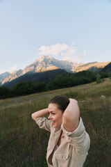 Fototapeta premium A woman enjoys an outdoor moment in a grassy field with distant mountains, light wind brushing her hair. A candid lifestyle image capturing natural joy and serene nature.