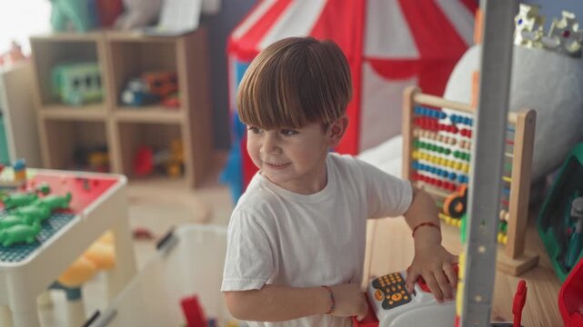 Boy playing with toy cash register and abacus pressing buttons and smiling inside building; curiosity joy.