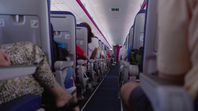 Inside airplane cabin view walking down aisle with passengers seated on both sides.