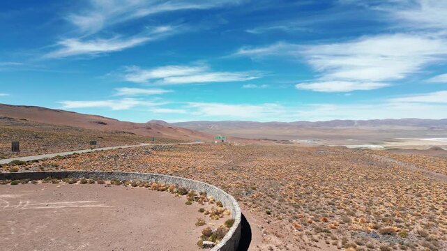 Forward flight over stone ruins of Paso Jama border checkpoint revealing vast arid plateau with salt lake and Andean mountain range under dramatic cloudy sky. Paso Jama, Chile
