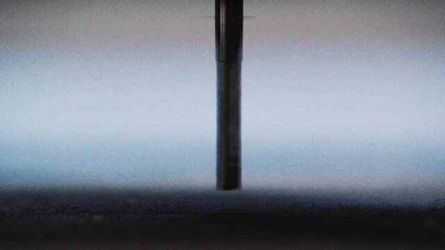 Minimal macro shot of a vertical end mill bit resting just above a flat material surface.