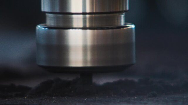 Macro shot of a CNC spindle cutting through dust and particles above a wooden surface.