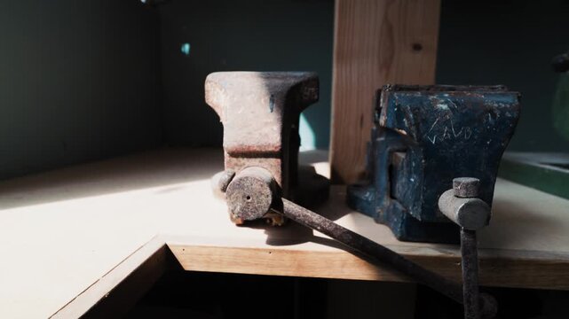 Bench vise mounted on a worktable with warm sunlight inside a woodworking workshop.