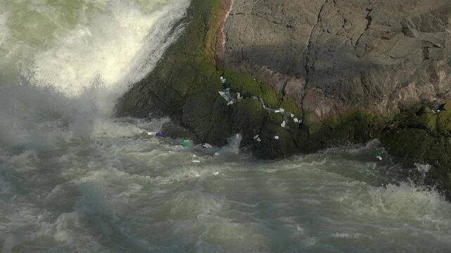 Slow motion close-up of plastic rubbish and foam being thrown around in the rapids at Li Phi Somphamit Falls, with litter trapped on the rocks in southern Laos.