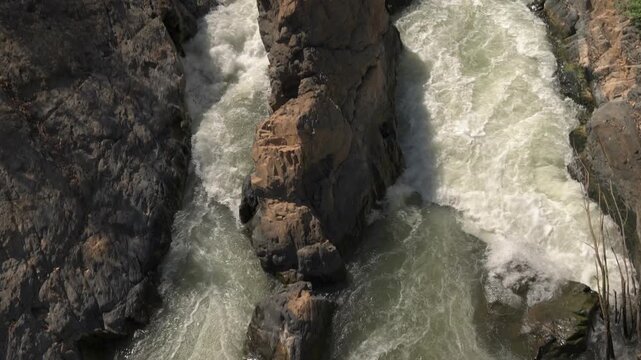 Top-down view of fast-flowing water splitting around rocks at Li Phi Somphamit Falls, tilting up to reveal the rocky downstream river channel on Don Khon, Laos.