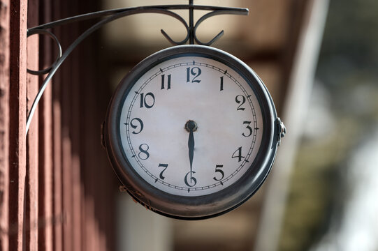 A vintage hanging clock is mounted outside a building with a softly blurred background