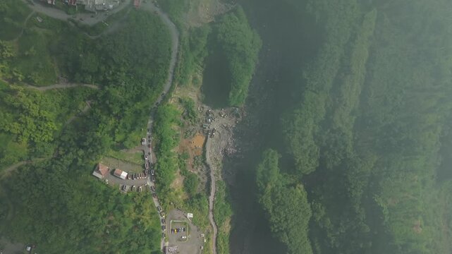 Aerial view of Tambang Pasir Merapi Kali Gendol Sand Mine with trucks and machinery surrounded by lush green hills in Kecamatan Cangkringan, Daerah Istimewa Yogya, Indonesia.
